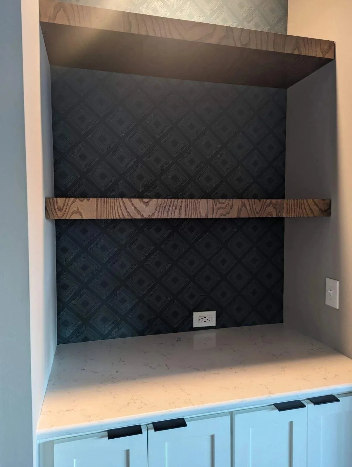 Floating wood shelves set into a papered alcove above custom base cabinets